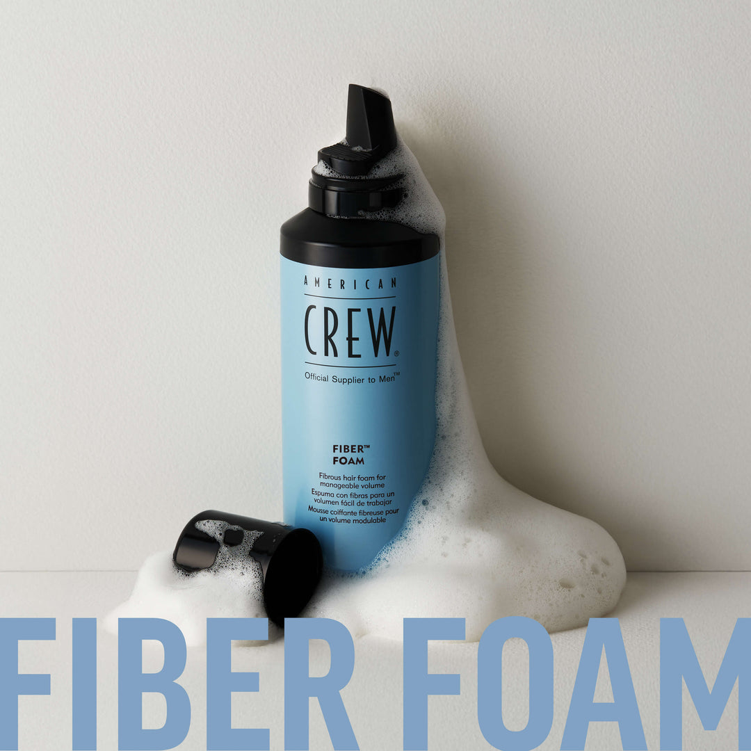 American Crew FiberGroming Foam with foamy bulk expelling and heaping around can and cap. Text on graphic states "Fiber Foam". 
