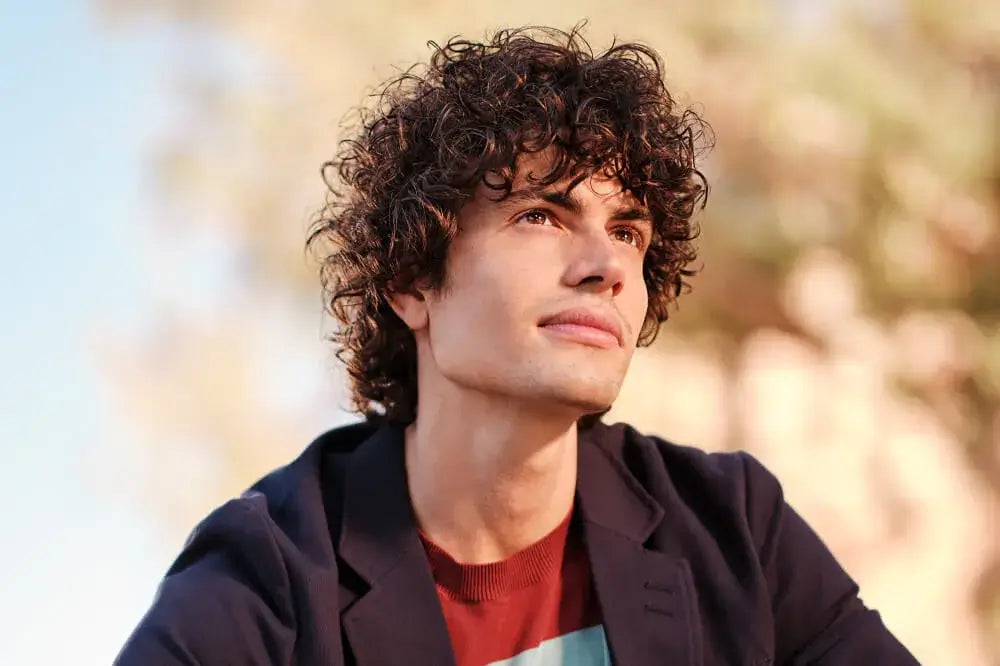 Discover Curly Hair Styling + Haircare recommendations from American Crew. Model seen smiling confidently facing the camera outdoors on a college campus.